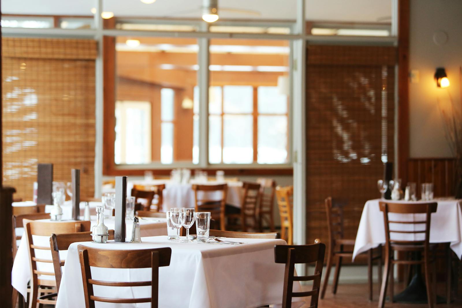 A serene restaurant interior with wooden chairs and tables set with glasses, ready for dining.